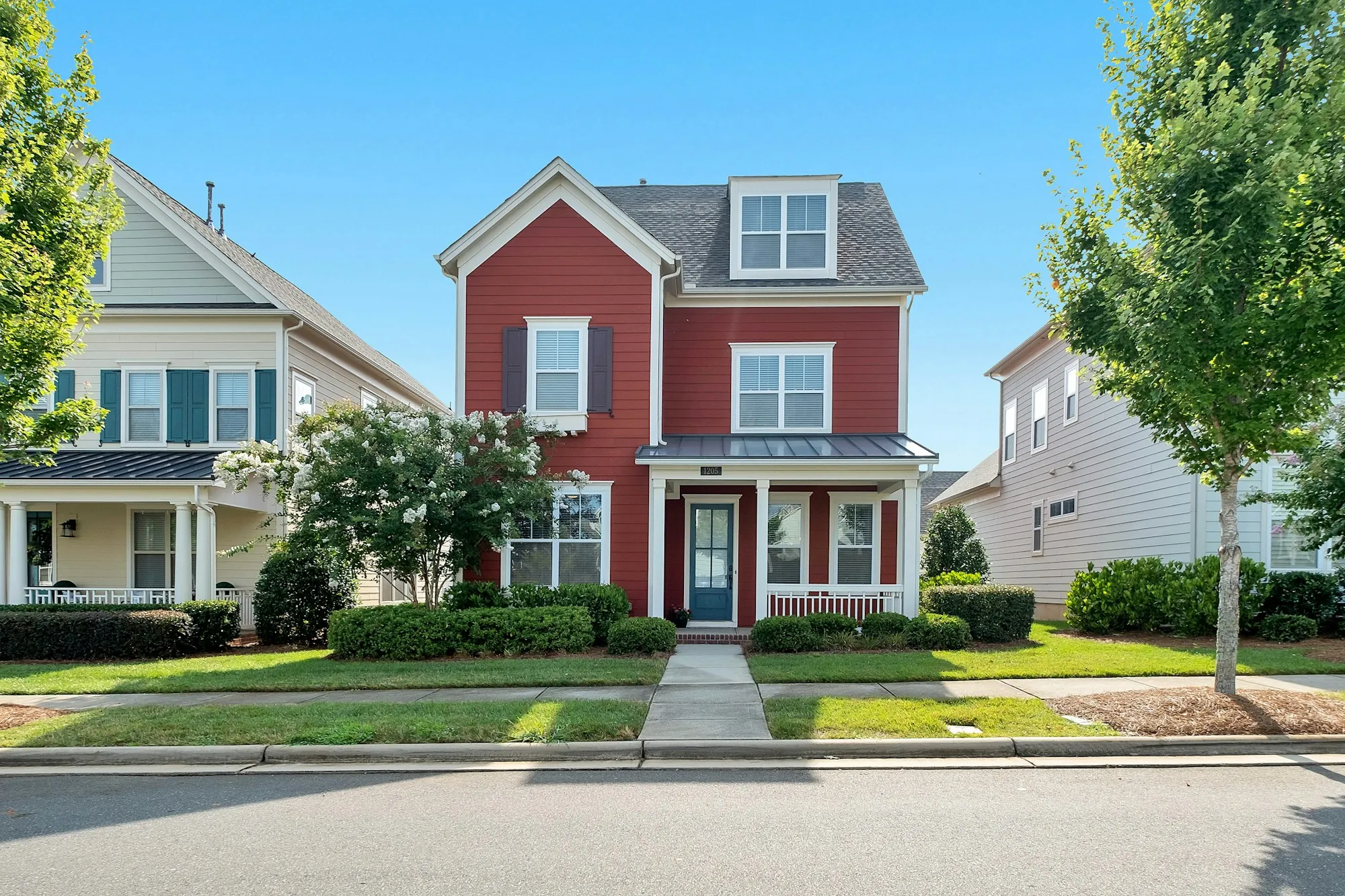 Red two-story house between neighbors on a suburban street