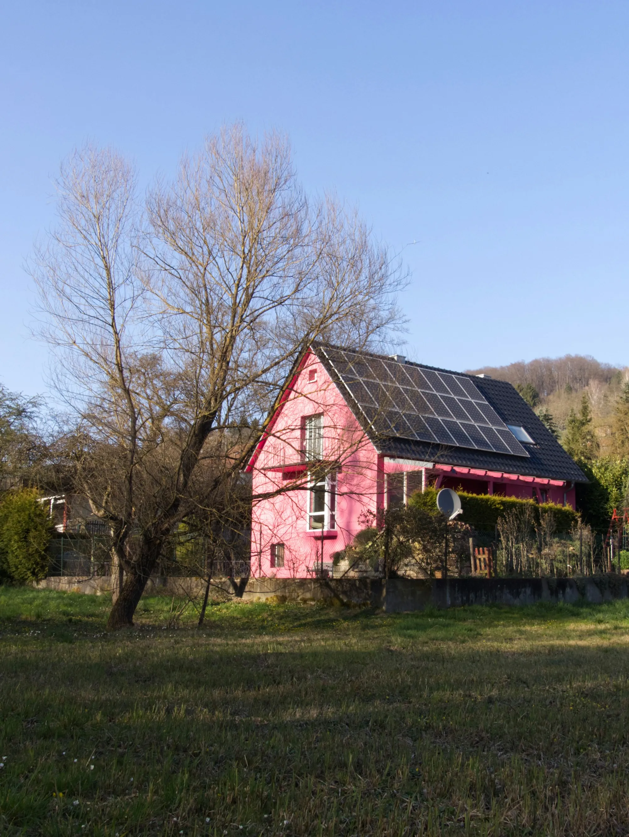 Pink two-story house with dark solar panels covering its roof