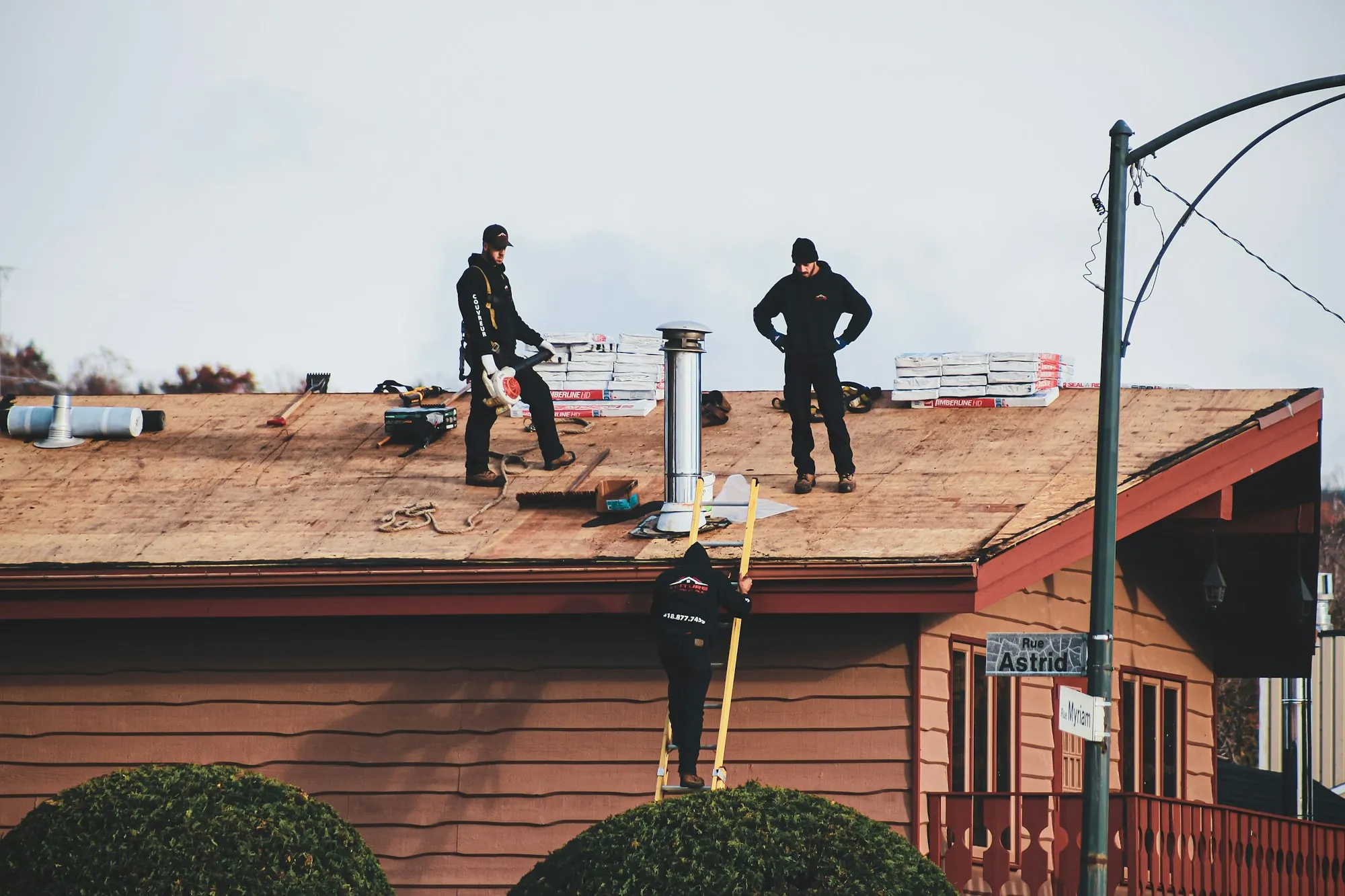Roofers working on a stripped roof deck of a red-sided house